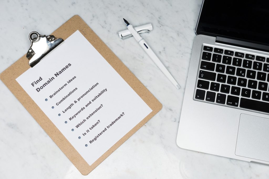 A clipboard, pen, and laptop on a white marble surface