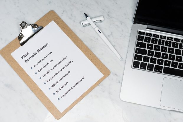 A clipboard, pen, and laptop on a white marble surface