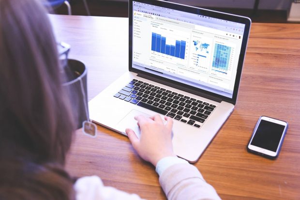 Woman using Google Analytics on a laptop. She is holding a cup of tea.