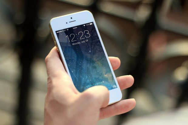 Hand holding a white iPhone. The home screen is on the screen