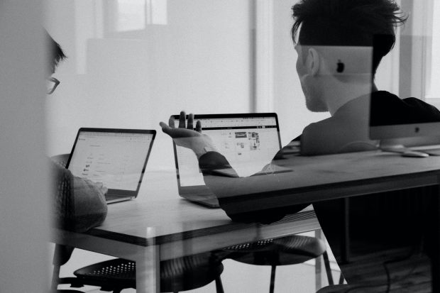Two men with laptops talking at a table
